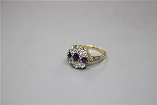 A Victorian style 18ct, three stone sapphire and six stone diamond set circular cluster ring, with diamond set shoulders,